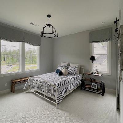 A Bedroom With Green-Tinged White Walls And White Ceiling, With A Bed And Small Furniture Items