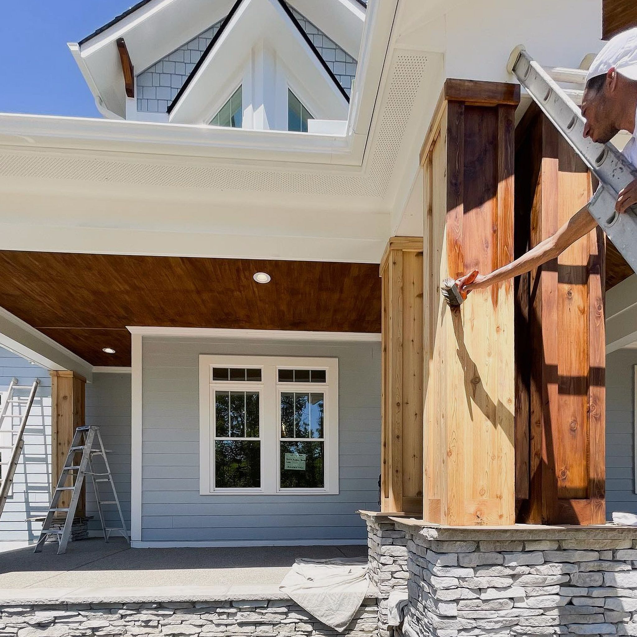 Wooden Pillars Are Being Painted By A Man On The Right And A Beautiful House On The Left - Lets Upgrade Painting