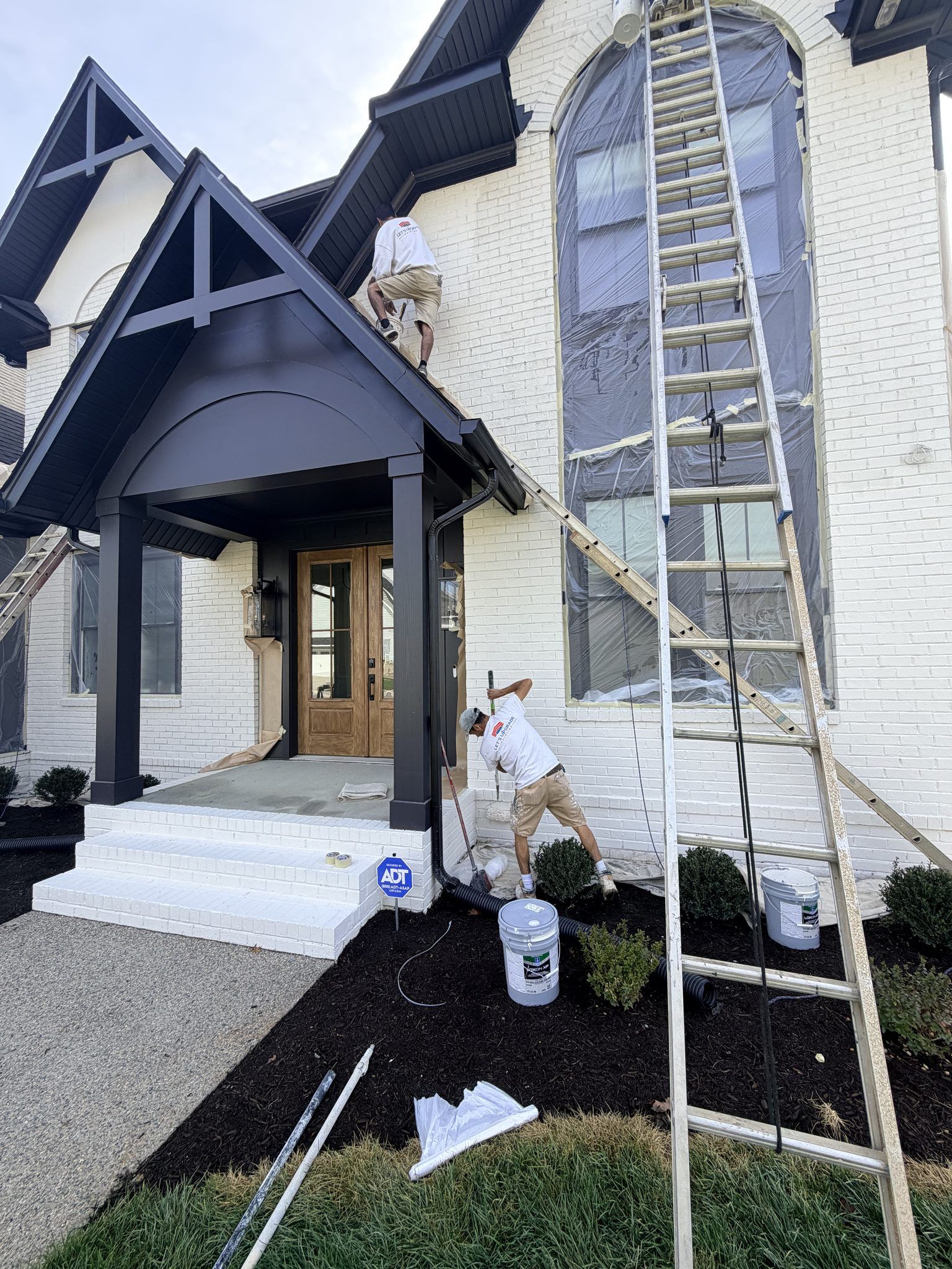 Painter On A Tall Ladder At The Entry Of A White Farmhouse