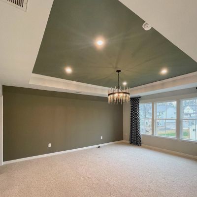 A Drawing Room With Hunter Green Color Ceiling And Walls With White Borders, A Light Grey Carpet, And A Few Slider Windows